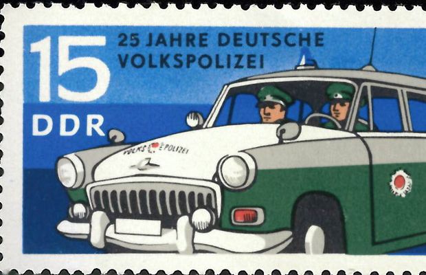Briefmarke der DDR mit Wert 15 Pfennige, die ein Auto der Deutschen Volkspolizei mit zwei Polizisten zeigt.