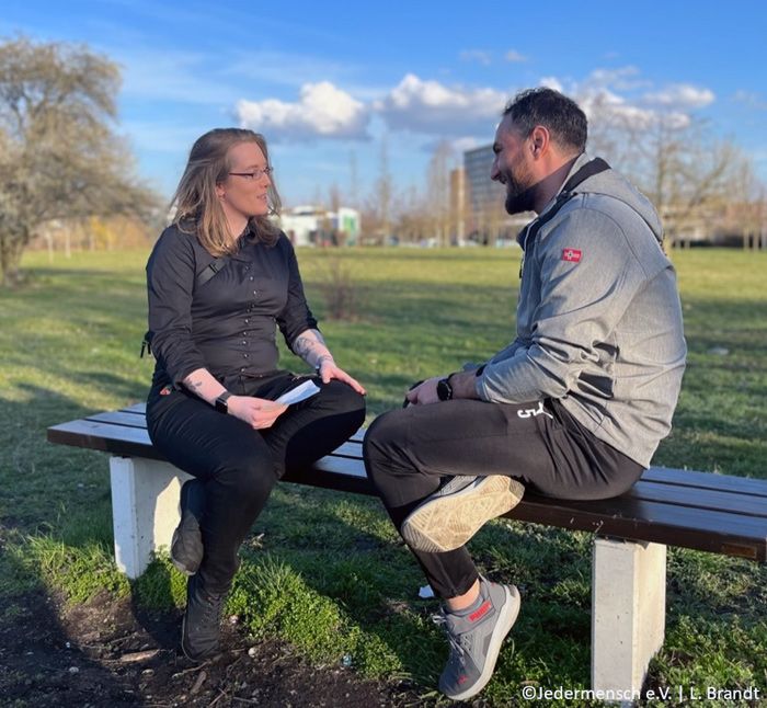 Zwei Personen sitzen im Park auf einer Bank und sprechen miteinander, im Rahmen der Living Library von Jedermensch e.V.
