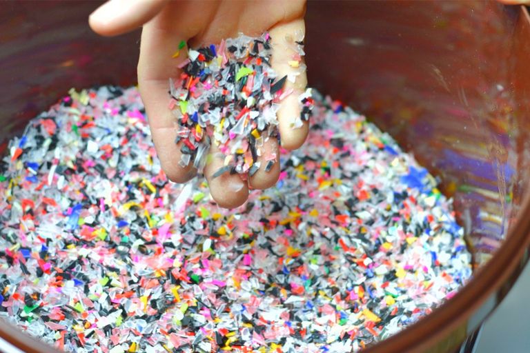 Eine Hand schöpft bunte Plastik-Teilchen aus einem Behälter.